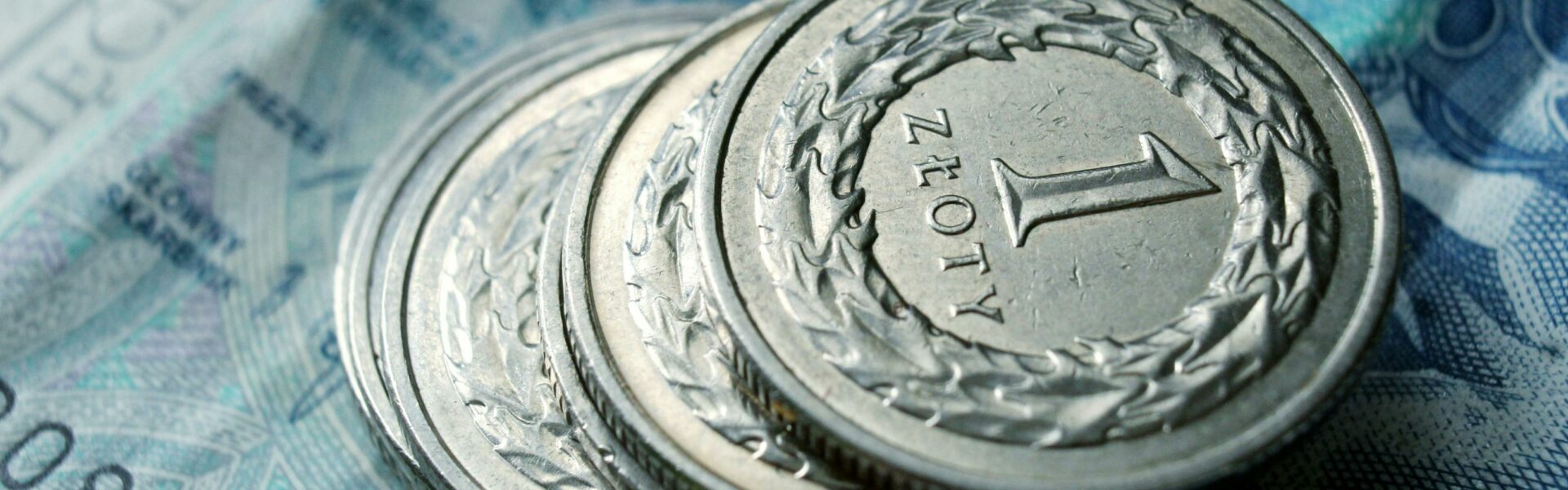 Stos srebrnych monet "1 złoty polski" położonych na niebieskim banknocie pięćdziesięciozłotowym
